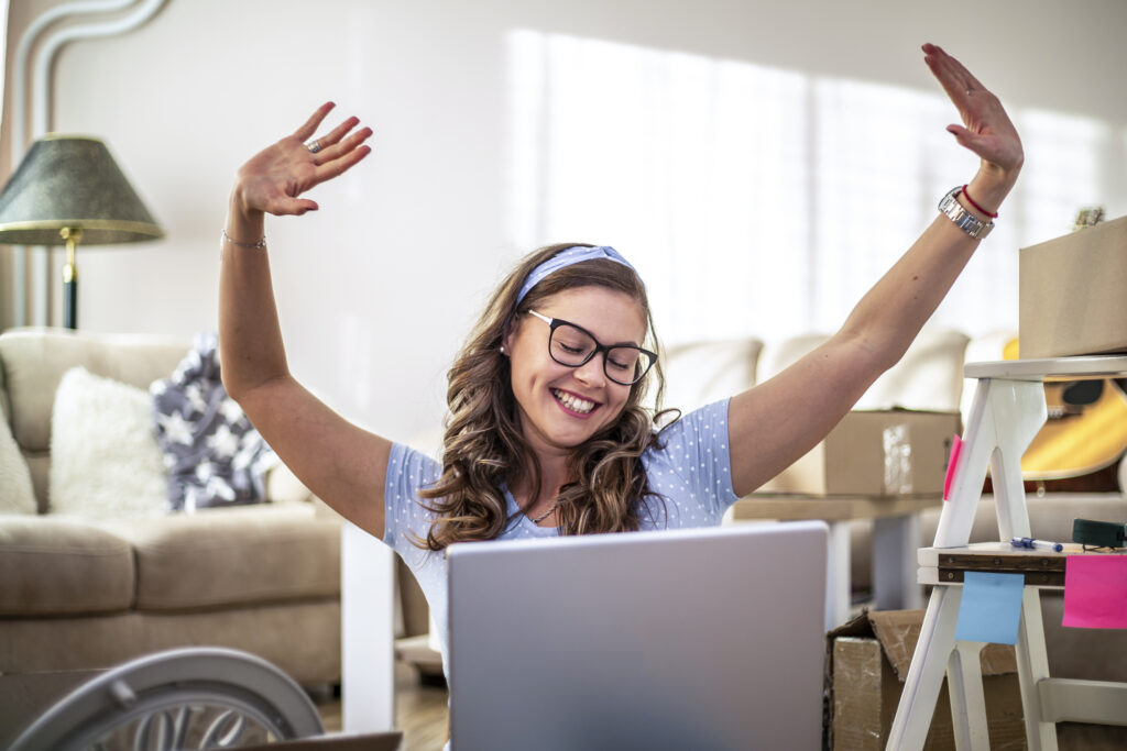 A young woman is sitting in a new apartment, she is happy in her new home. A young beautiful happy woman is unpacking boxes, she has just moved, she is sitting on the floor.