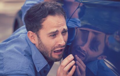 Frustrated upset young man looking at scratches and dents on his car outdoors