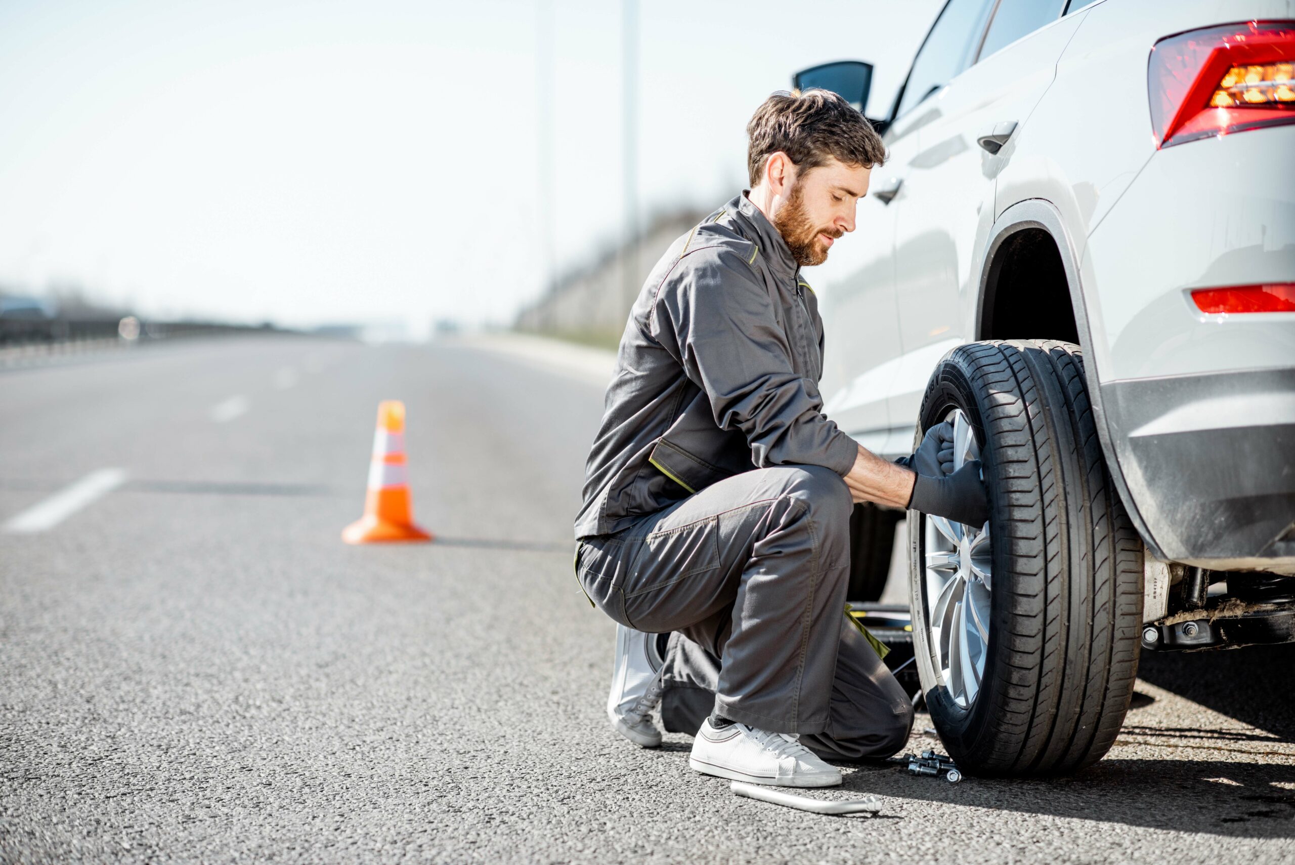 Handsome road assistance worker in uniform changing car wheel on the highway